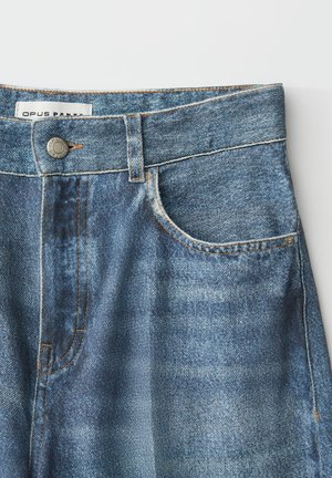 Blauwe spijkerbroek met voorzak, riemlussen, metalen knoop en zichtbare steeknaden, plat gelegd op een witte achtergrond.