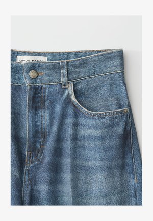 Blauwe spijkerbroek met voorzak, riemlussen, metalen knoop en zichtbare steeknaden, plat gelegd op een witte achtergrond.