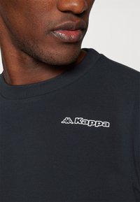 Zwarte katoen T-shirt met ronde hals, gestructureerde stof en een wit Kappa-logo op de linkerborst.