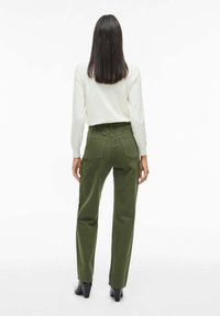 Pantalones verdes con un corte recto, dos bolsillos traseros y una cintura alta. La tela parece suave con un ligero brillo. Se llevan con un suéter beige.