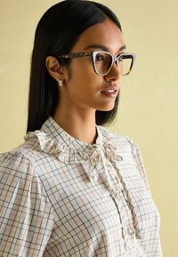 Schildpattmuster Eyegläser mit klaren Rahmen, getragen mit einer rüschigen, cremefarbenen Karobluse mit blauen und rosa Linien.