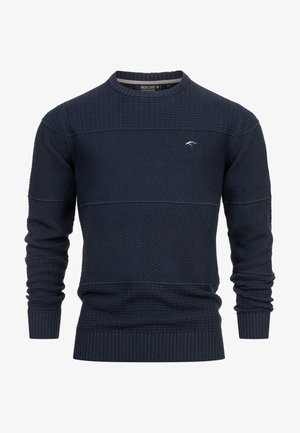 Laivastonsininen neulepusero, jossa on texturoituja kuvioita, pyöreä kaula-aukko ja resorit. Rinnassa on hienovarainen logo ja paksu lanka.