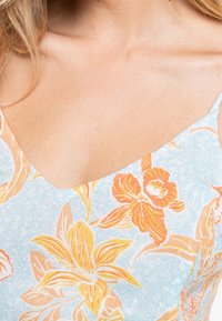 Kukkaprintinen mekko, jossa vaaleansininen tausta, oranssit ja keltaiset kukat, v-mallinen pääntie ja ohuet olkaimet.