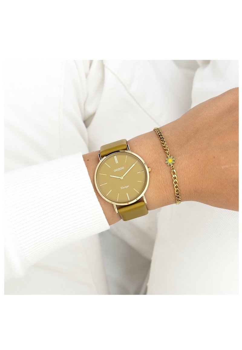 Montre Oozoo avec un boîtier rond en acier doré, un bracelet en cuir vert olive et un cadran minimaliste avec des index et des aiguilles dorées.