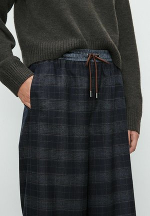 Marineblauwe geruite broek met een elastische tailleband, voorzien van een bruine trekkoord en zijzakken. Gemaakt van een zachte, gestructureerde stof.