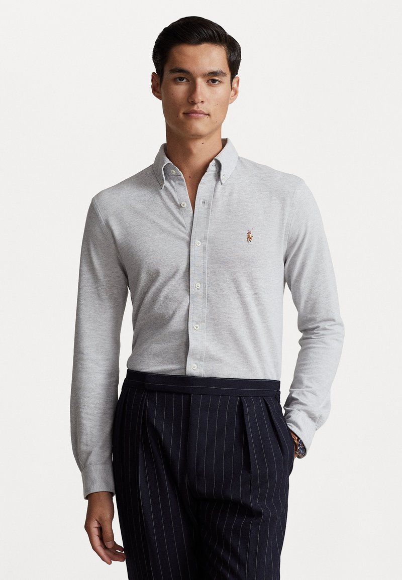 Light gray long-sleeve button-up shirt with a collar and small logo, paired with dark pinstripe trousers. Smooth fabric, tailored fit.