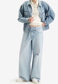 Giacca di jeans azzurro chiaro con una vestibilità rilassata, abbinata a jeans azzurro chiaro a gamba larga con vita regolabile e un dettaglio strappato.