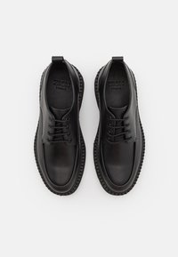 Scarpe in pelle nera con punta arrotondata, design con lacci e suola in gomma texturizzata. Presenta il logo impresso sulla soletta e linguette per il trasporto.