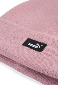 Világos rózsaszín kötött sapka hajtott mandzsettával, fekete téglalap alakú címkével, fehér "PUMA" felirattal és logóval. Puha textúra.