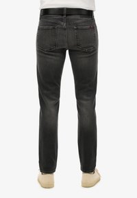 Jeans de mezclilla negra con corte recto, que cuentan con dos bolsillos traseros y un acabado limpio. Llevados con un cinturón negro y zapatos de color claro.