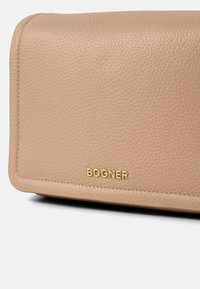 Portafoglio in pelle beige con una superficie liscia e testurizzata. Presenta la scritta in oro "BOGNER" sul fondo, con bordi cuciti in modo ordinato.