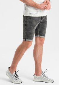 Harmaat denim-shorts käännetyillä hempeillä ja slim fit -mallilla, yhdistettynä kevyisiin valkoisiin verkkokenkiin, joissa on mustat nauhat ja yksityiskohdat.