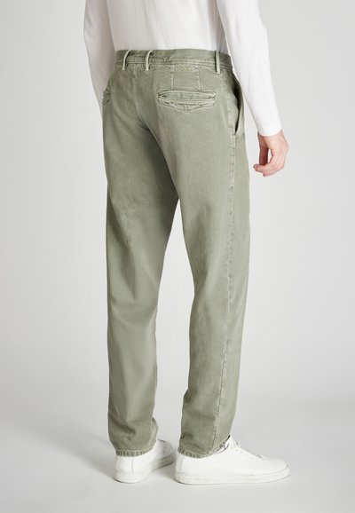 Lichtgroene, loszittende broek van een textuurstof, met twee achterzakken en een omgeslagen zoom, gecombineerd met witte sneakers.