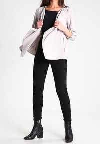 Veste gris clair à fermeture éclair, haut noir, jean skinny noir et bottines à talons noires. Le tissu semble lisse avec peu de détails.