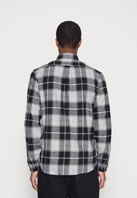 Černo-bílá kostkovaná košile s dlouhými rukávy, límcem na knoflíky a zakřiveným lemem, vyrobená z měkké, strukturované tkaniny.