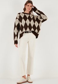 Rjav in smetanasto bež argyle pulover z spuštenimi rameni in rebrastimi manšetami, v kombinaciji z belimi hlačami z višjim pasom in bež supergami.