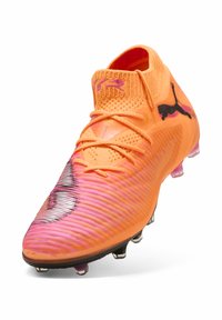 Kirkkaan oranssi jalkapallokengän yläosa on teksturoitu, siinä on dynaamisia vaaleanpunaisia yksityiskohtia, musta logo ja näkyvät nastat pitoa varten. Nauhallinen malli.
