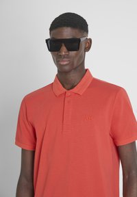 Koraalkleurig polo shirt met korte mouwen van katoen, met een kraag, een drievoudige knoopsluiting en een geborduurd logo op de borst.