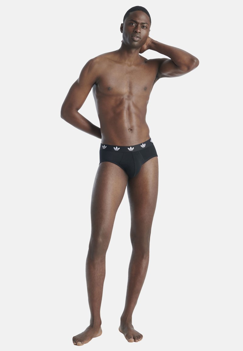 Zwarte katoenen boxershorts met een elastische tailleband met drie witte Adidas-logo's. Het model staat met één hand achter zijn hoofd en de voeten uit elkaar.