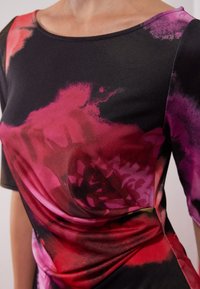 Schwarzes Kleidungsstück mit floralem Design in Farbtönen von Pink, Lila und Rot. Verfügt über einen runden Ausschnitt und eine weiche, glatte Textur.