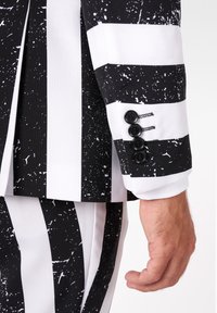 Čierno-biely pruhovaný oblek s bodkovaným vzorom; detail na rukáve saka, so štyrmi čiernymi gombíkmi na manžete.