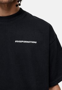 Zwarte katoenen T-shirt met korte mouwen, met een wit logo dat "GOODFOR NOTHING" over de borst toont in een vet, modern lettertype.