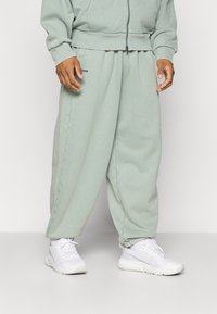 Ljusgröna sweatpants med en avslappnad passform, utrustade med ribbade muddar och en liten logotypdetalj. Matchas med vita träningsskor.