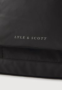 Juodas audinys maišas, turintis tekstūruotą paviršių, horizontalų dizainą ir sidabrinį "LYLE & SCOTT" logotipą priekyje.