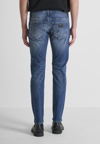 Plave traperice uskog kroja; imaju dva stražnja džepa, zakrpu s logotipom na pojasu i blago izblijedjeli završni sloj.