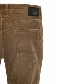 Bruine corduroy broek met een gestructureerde afwerking, voorzien van een opvallende achterzakstijl en een zwart label met "camel active" branding.