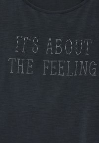 Tmavě modré měkké tričko s kulatým výstřihem, které má výrazný bílý text s ozdobnými kamínky: "ZA TO STOJÍ POCIT".