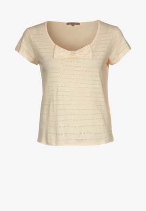 Vaalean beige paita, jossa on pyöreä pääntie, lyhyet hihat ja etuosassa nauhakiinnitys; siinä on pystysuoria ja vaakasuoria leikkauksia.