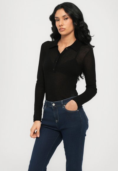 Camisa polo negra de manga larga en una tela ligera y traslúcida, con collar y cierre de botones, combinada con jeans de tiro alto en azul oscuro.
