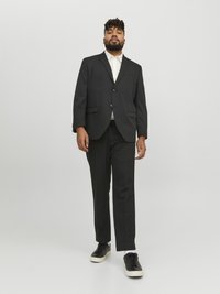 Black suit with single button closure and notch lapels, paired with a light-colored shirt and black sneakers. Smooth textures and tailored fit.