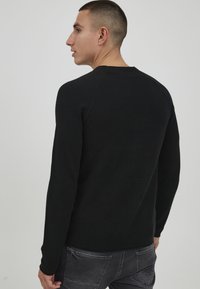 Zwarte langemouwt-shirt met een gestructureerd oppervlak, ronde halslijn en raglanmouwen, gecombineerd met donkergrijze broek.