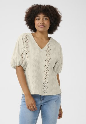 Light beige blouse with a V-neck, textured fabric, short puffed sleeves, and zigzag cut-out patterns along the sides.