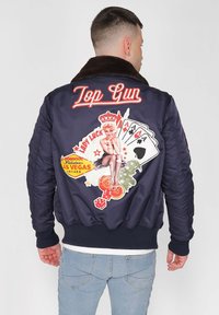 Marineblaues Bomberjackett mit Kunstfellkragen, verziert mit bunten, gestickten Patches von Spielkarten, Würfeln und einem Pin-up-Mädchen.