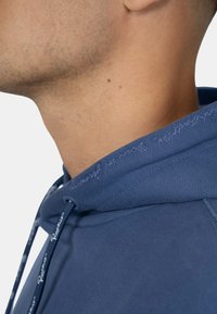 Felpa con cappuccio blu navy dotata di coulisse, con una texture morbida. Il bordo del cappuccio presenta del testo ricamato in un colore chiaro a contrasto.