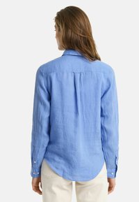 Lichtblauw, langärmelig linnen shirt met een button-down kraag, een gebogen zoom en subtiele textuur, met knoopdetails op de mouwen.