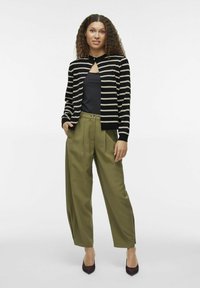 Melna un krēmkrāsas svītrainā kardigāna ar atslēgu caurumu, apvienots ar augsto jostasvietu olīvu zaļiem biksēm un smailiem brūniem apaviem.