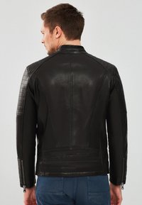 Zwarte leren jas met een slim-fit ontwerp, doorgestikte schouderdetails en ritsmanchetten. Smooth textuur en minimalistische stijl.