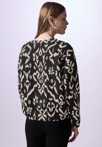 Top a maniche lunghe con motivo nero e crema, dal taglio rilassato, con scollatura rotonda e spalle leggermente abbassate. Tessuto morbido al tatto.