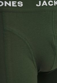 Dunkelgrüne Herrenunterwäsche mit einem weißen Markenbund, aus weichem Baumwollmaterial und einem körpernahen Schnitt mit nahtloser Verarbeitung.