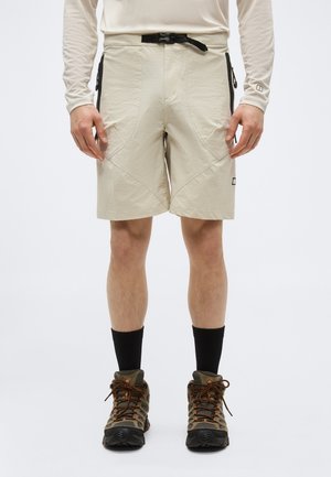 Beige Outdoor-Shorts mit Vordertaschen, einem schwarzen verstellbaren Gurtschnallen, getragen mit schwarzen Socken und braunen Wanderschuhen.