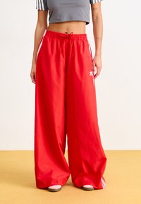 Pantalons larges rouges en tissu léger, dotés d'une taille à cordon, de rayures blanches discrètes et d'un logo sur le devant.