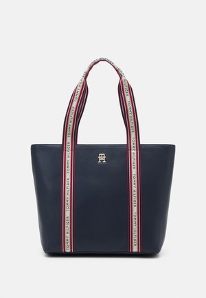 Marineblaue Tragetasche mit langen Stoffgriffen mit roten, weißen und blauen Streifen und dem Schriftzug „Tommy Hilfiger“ entlang der Träger.