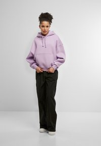 Lilla overdimensjonert hettegenser med frontlomme, sammen med svarte cargo-bukser. Antrekket har en avslappet passform og elastiske mansjetter. Hvite sneakers fullfører stilen.