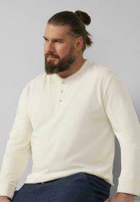 Crème lange mouwen henley-shirt met vier houten knopen, ribgebreide manchetten en een textuurstof. Gekocht met donkerblauwe broeken.
