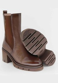 Stivali alla caviglia in pelle marrone con finitura texturizzata, tacco a blocco, pannelli elastici laterali e suola in gomma con una decorazione a tasselli.