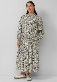 Abito lungo con stampa leopardata, dotato di bottoni sul davanti, colletto, maniche lunghe e orlo a strati. Abbinato a sneakers bianche e beige.